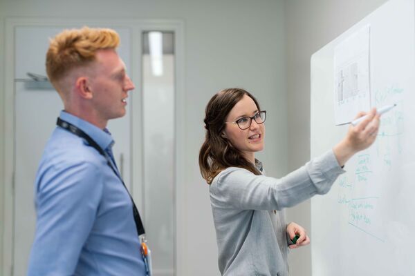 Zwei Personen diskutieren vor einem Whiteboard.