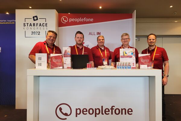 peoplefone Mitarbeiter am Stand schauen in die Kamera. Im Hintergrund steht eine Messewand.
