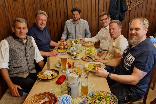 Mehrere Personen sitzen an einem Holztisch und unterhalten sich - Stammtisch München.